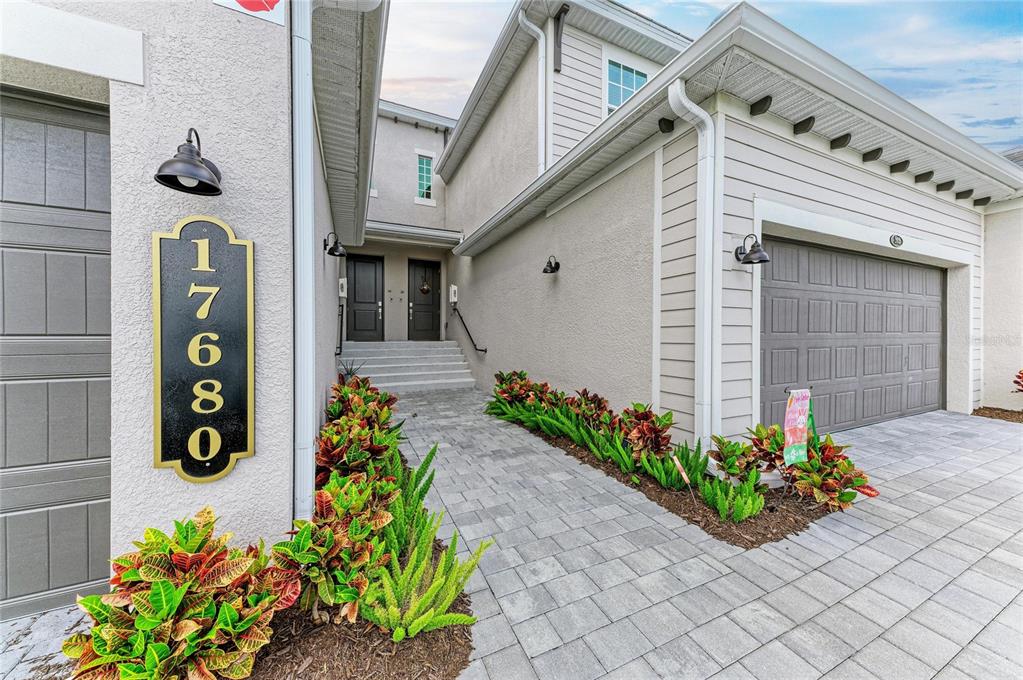 The exterior of a two-story home features a paved walkway, landscaping, and two garage doors — 17680 BORACAY COURT UNIT 202, VENICE, FL