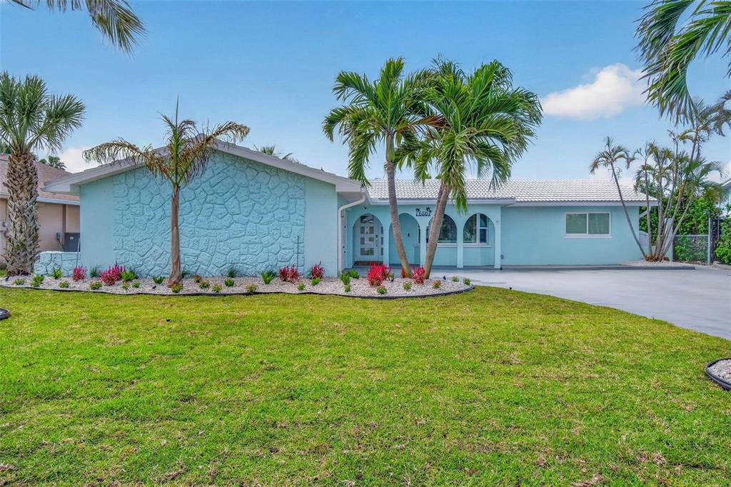 A light blue, single-story house features a stone facade, palm trees, and a concrete driveway — 650 64TH AVENUE, ST PETE BEACH, FL