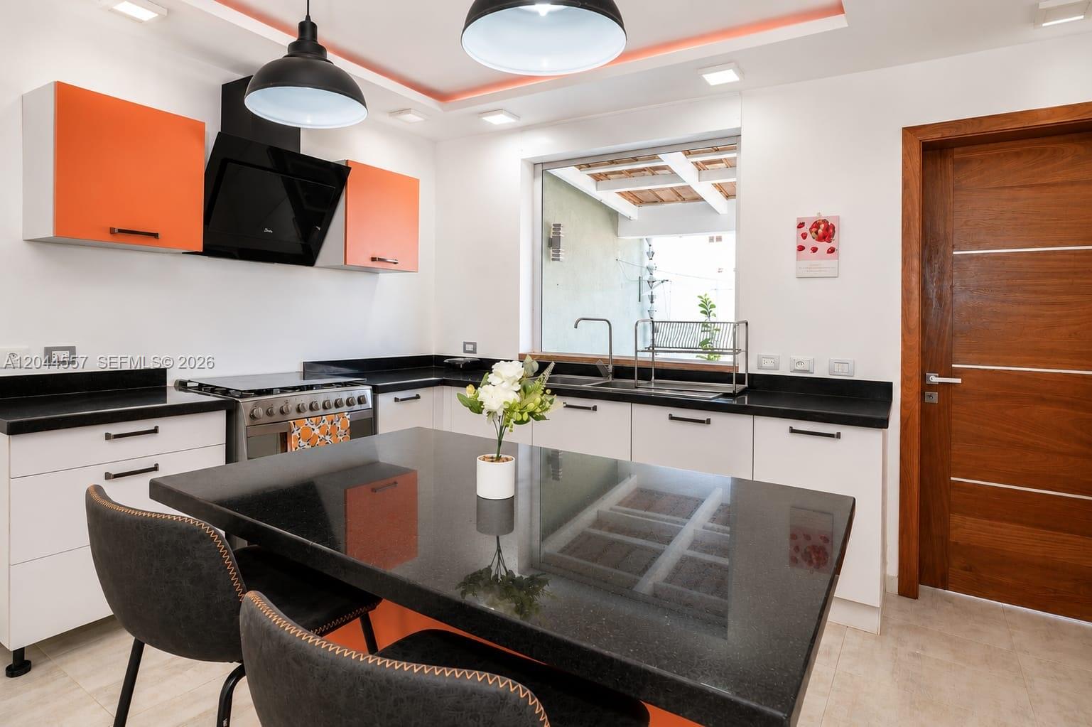 A modern kitchen features orange upper cabinets, white lower cabinets, black countertops, and a central island — FL