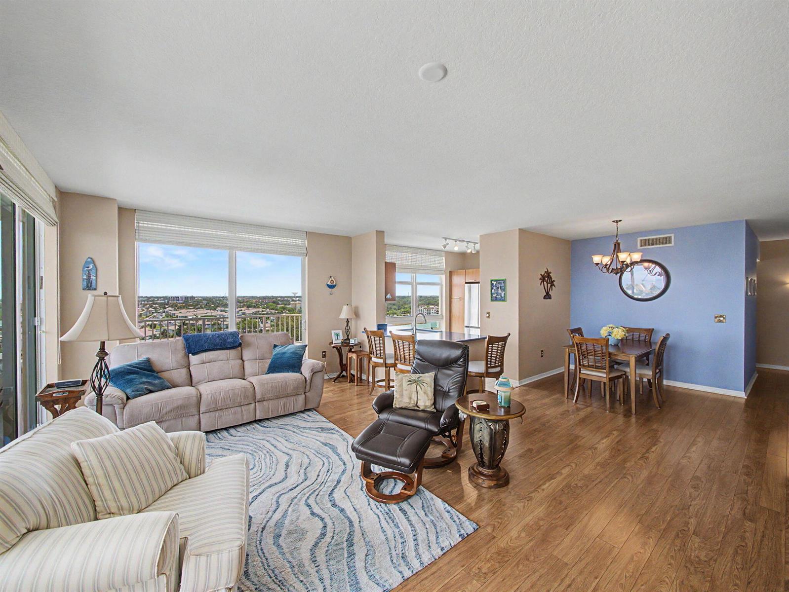 An open-concept living and dining area with hardwood floors, a blue accent wall, and balcony views — 625 Casa Loma Boulevard # 1402, Boynton Beach FL 33435, BOYNTON BEACH, FL
