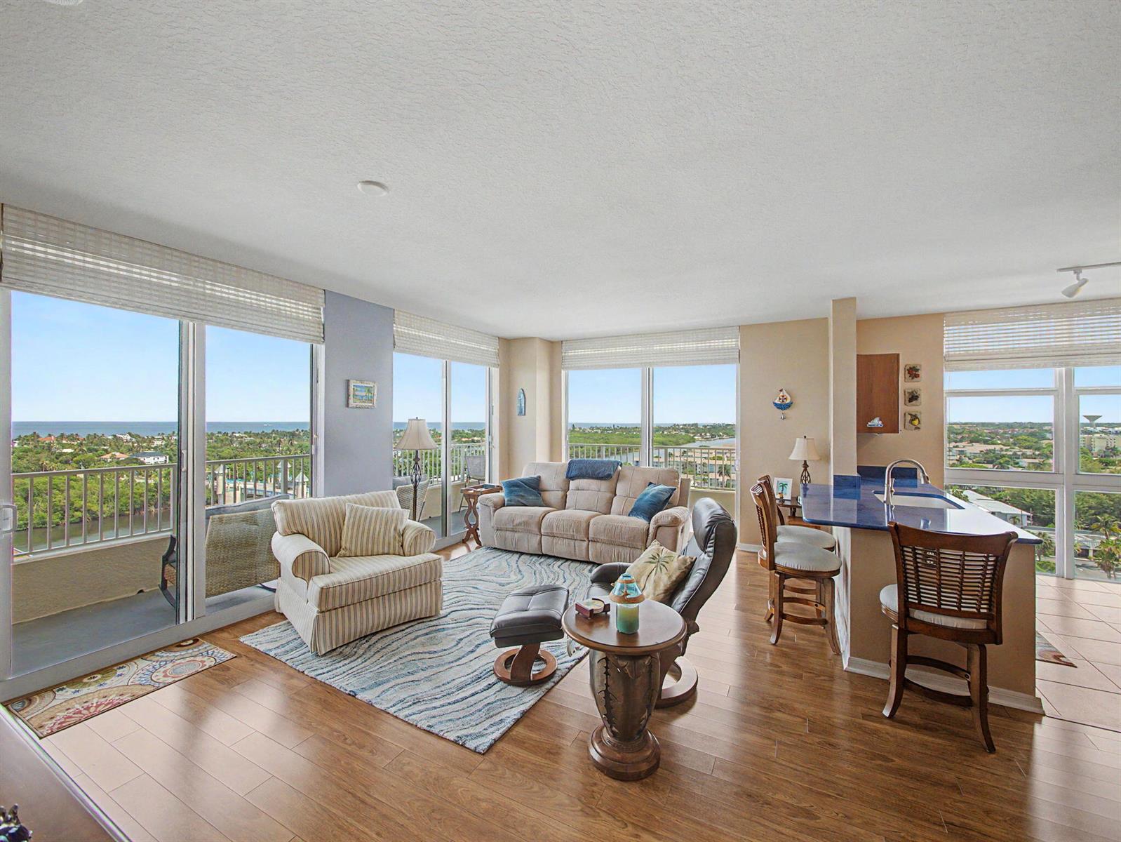 A living room with hardwood floors, a blue area rug, and floor-to-ceiling windows overlooking water — 625 Casa Loma Boulevard # 1402, Boynton Beach FL 33435, BOYNTON BEACH, FL