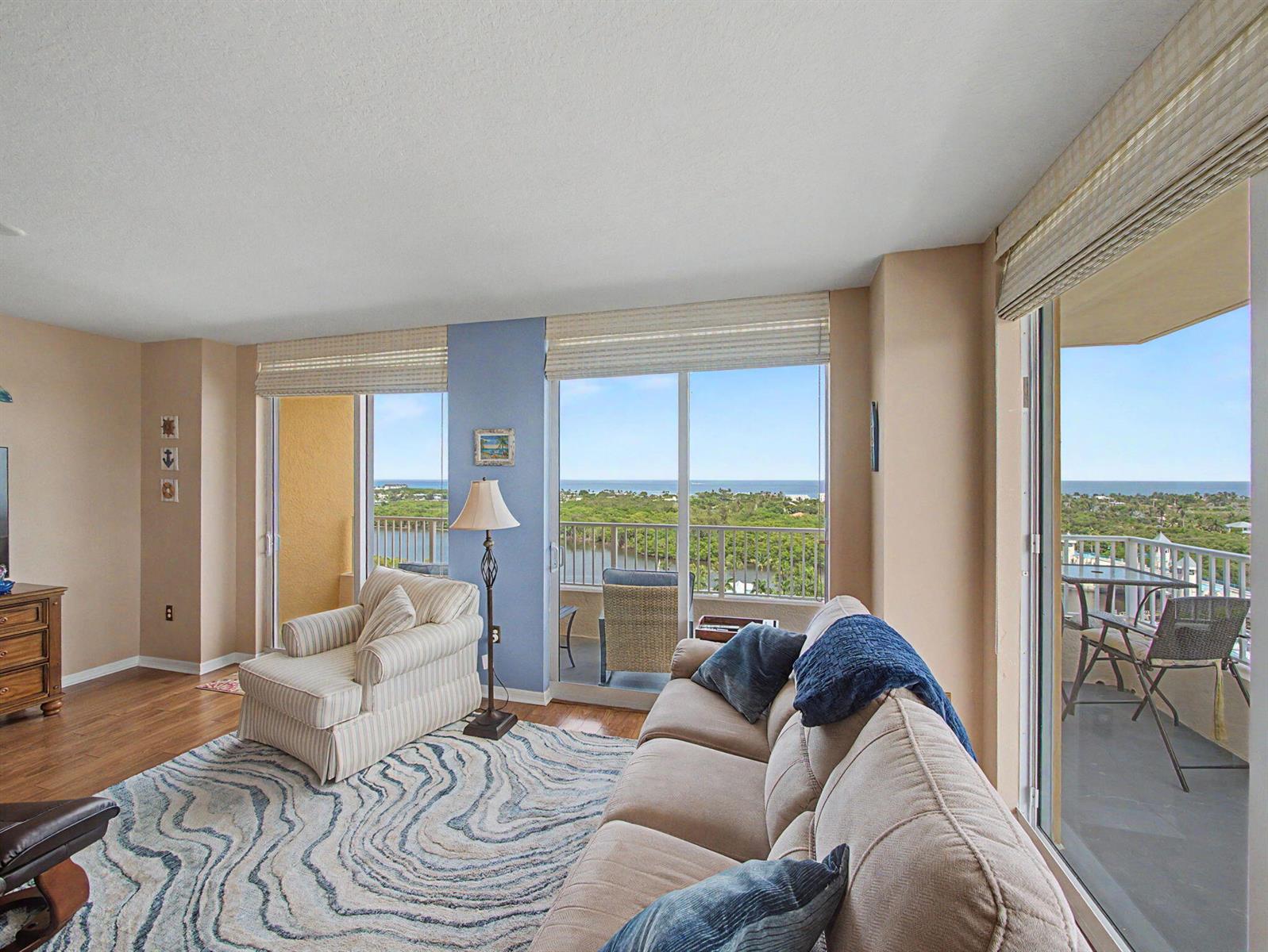 A living room with a beige sofa, striped armchair, and balconies overlooking the ocean — 625 Casa Loma Boulevard # 1402, Boynton Beach FL 33435, BOYNTON BEACH, FL