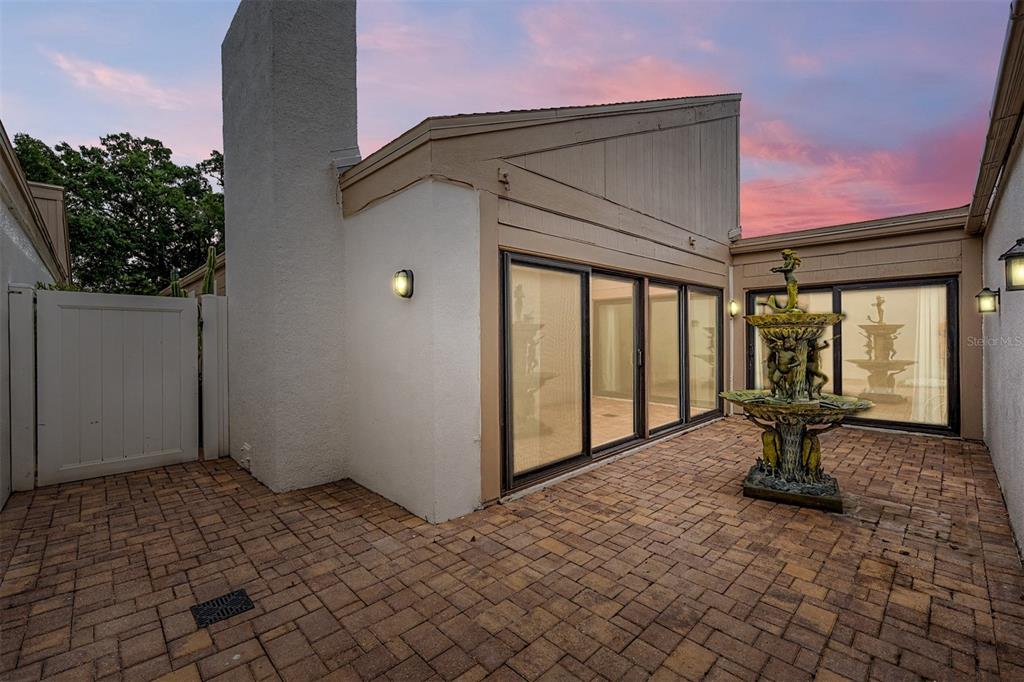 A paved patio features a tiered fountain and sliding glass doors leading into the home — 360 S WOODLANDS DRIVE, OLDSMAR, FL