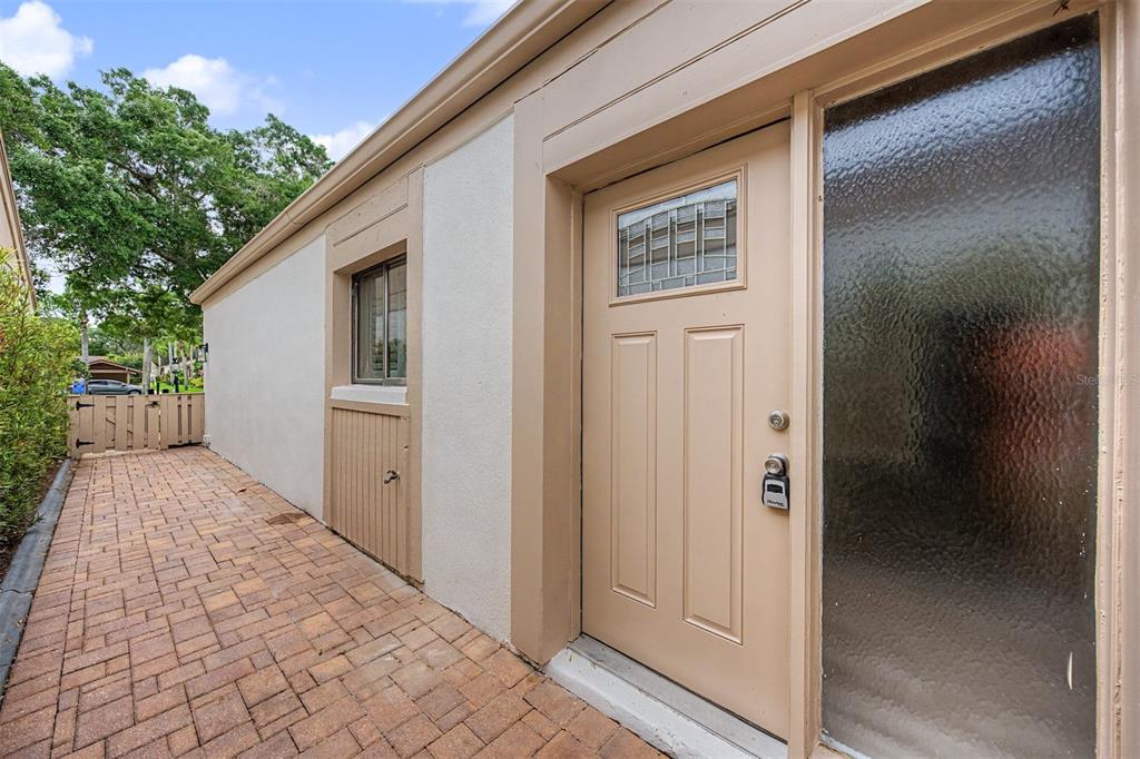 A tan exterior door with a small window sits beside a window on a brick patio — 360 S WOODLANDS DRIVE, OLDSMAR, FL
