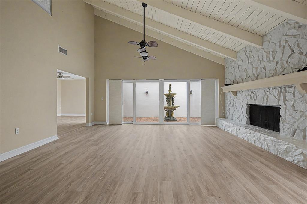 A living room with vaulted ceilings, wood-look flooring, a stone fireplace, and sliding glass doors — 360 S WOODLANDS DRIVE, OLDSMAR, FL