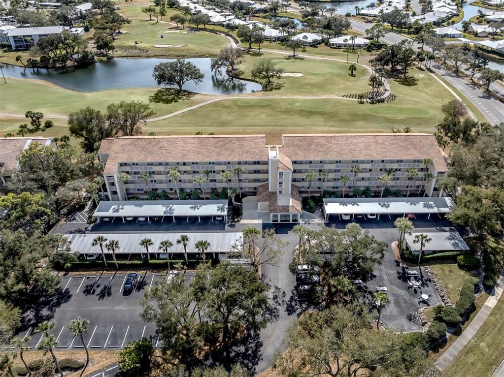 An aerial view shows a multi-story apartment building with covered parking and a golf course — 818 WEXFORD BOULEVARD UNIT 818, VENICE, FL