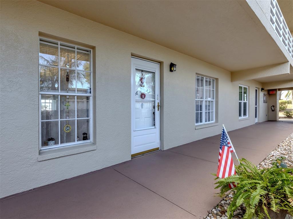 A beige building exterior features a white front door, two windows, and a small American flag — 818 WEXFORD BOULEVARD UNIT 818, VENICE, FL