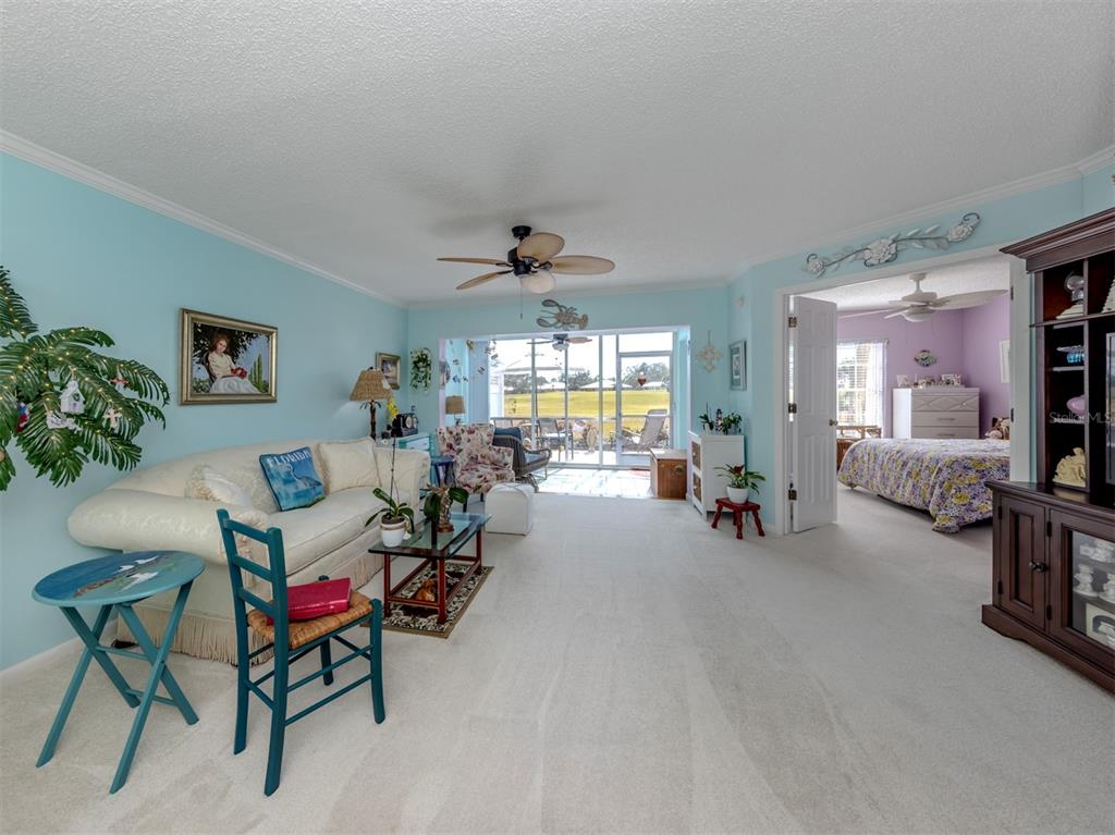 A living room with light blue walls, carpeted floors, and an adjacent bedroom visible through doors — 818 WEXFORD BOULEVARD UNIT 818, VENICE, FL