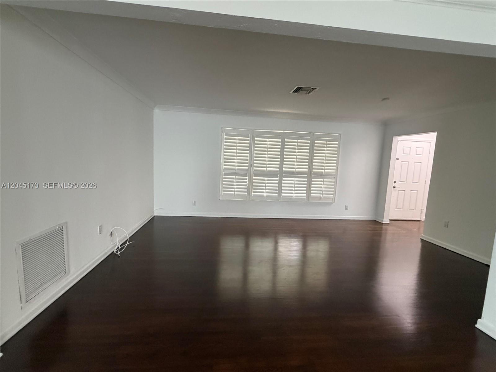 An empty room features dark hardwood floors, white walls, and a large window with shutters — 1420 Baracoa Ave, Coral Gables FL 33146, CORAL GABLES, FL
