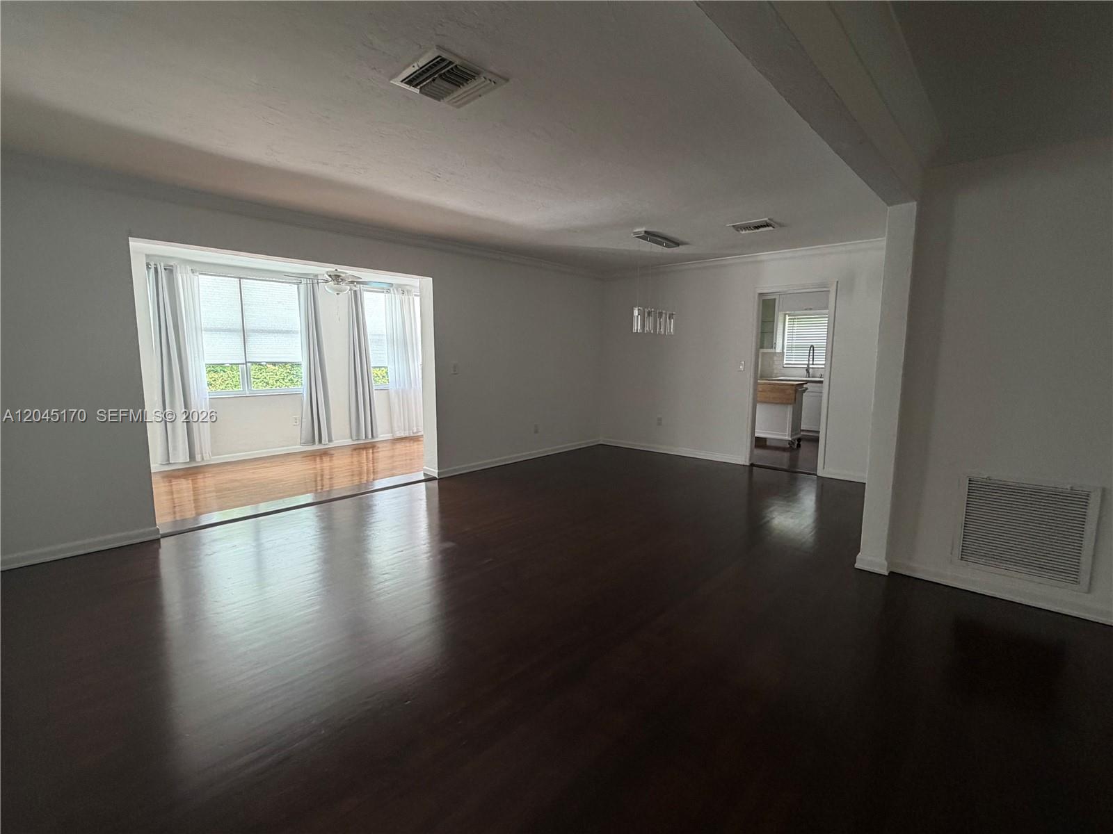 A spacious living room features dark hardwood floors, white walls, and an adjacent sunroom — 1420 Baracoa Ave, Coral Gables FL 33146, CORAL GABLES, FL