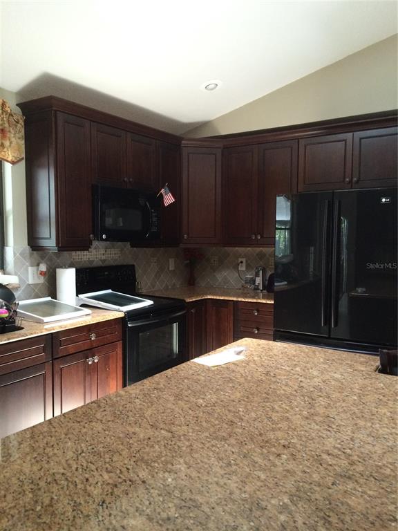 A kitchen features dark wood cabinets, granite countertops, and black appliances — 1114 SEAFARER LANE, WINTER SPRINGS, FL