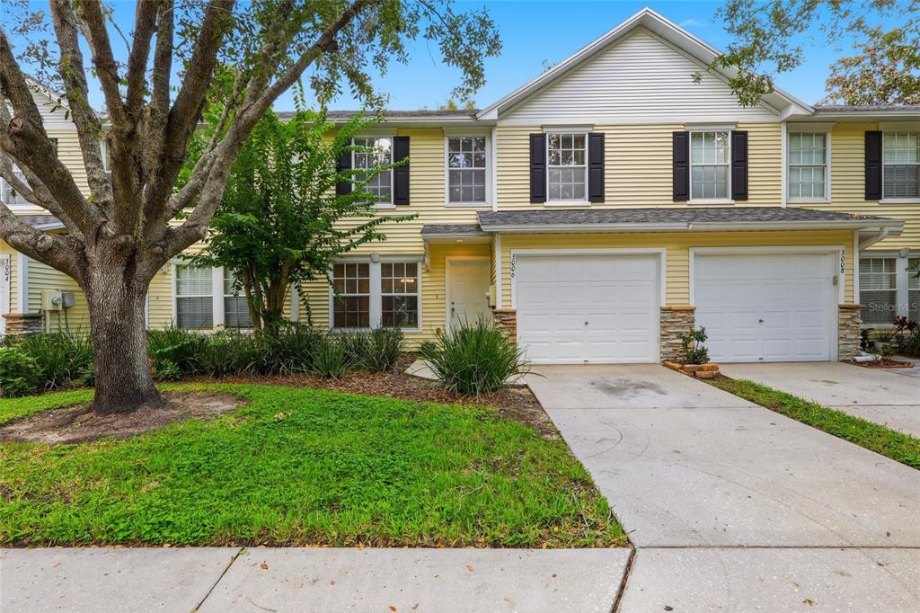 A two-story yellow townhouse with a white garage, stone accents, and a front lawn — 3006 AMBER OAK DRIVE, VALRICO, FL