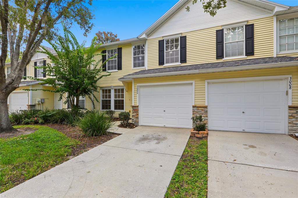 A two-story yellow townhouse with white garage doors and a concrete driveway — 3006 AMBER OAK DRIVE, VALRICO, FL