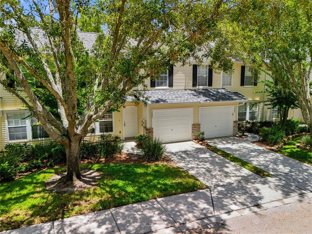 A two-story yellow townhouse with two garage doors and a large tree in front — 3006 AMBER OAK DRIVE, VALRICO, FL