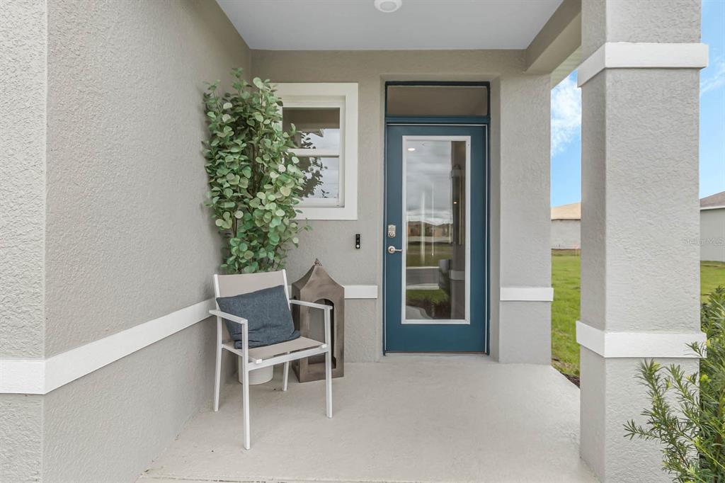 A covered front porch features a blue glass-paneled door, a chair, and a potted plant — 3375 PINE LILY AVENUE, POINCIANA, FL