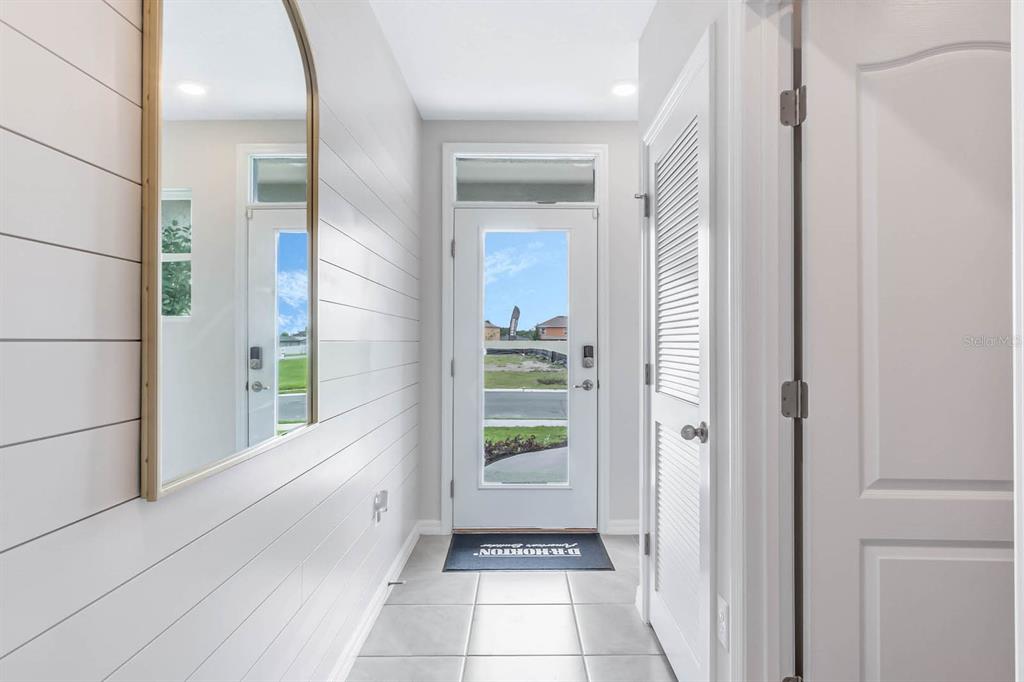 An entryway features white shiplap walls, a large arched mirror, and a glass-paneled front door — 3375 PINE LILY AVENUE, POINCIANA, FL