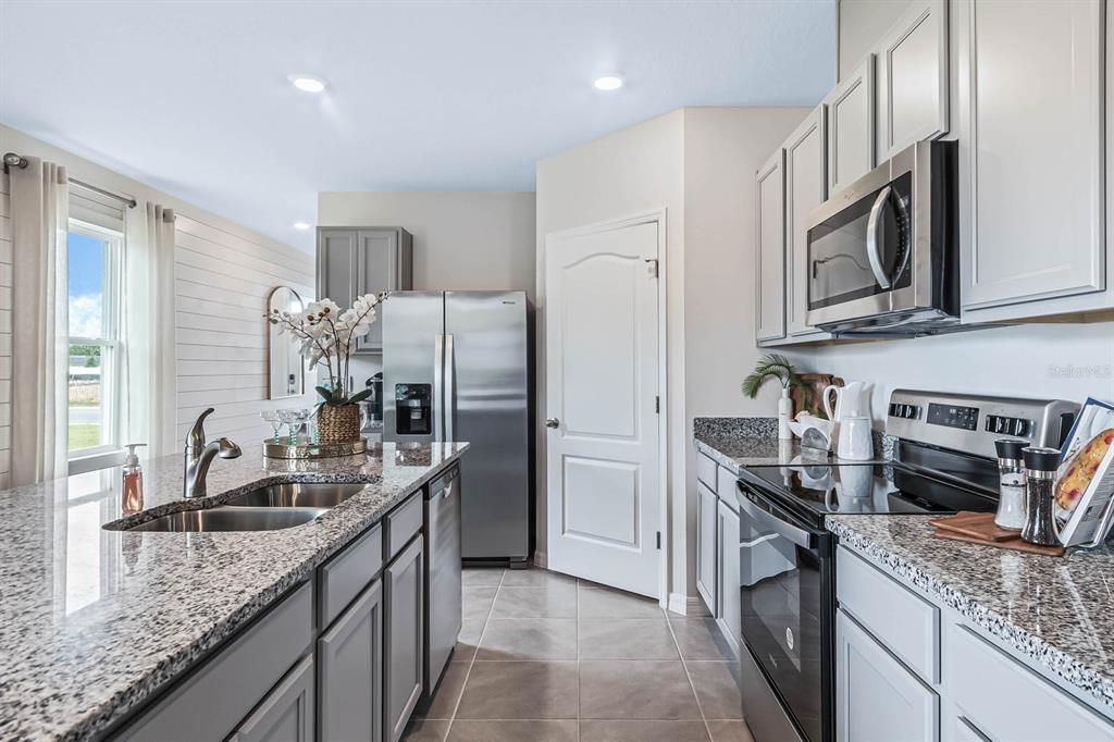 A kitchen with gray cabinets, granite countertops, stainless steel appliances, and a tile floor — 3375 PINE LILY AVENUE, POINCIANA, FL