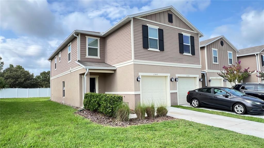 A two-story townhouse with beige siding, a tan stucco lower level, and two garage doors — 1340 MIRABELLA CIRCLE, DAVENPORT, FL