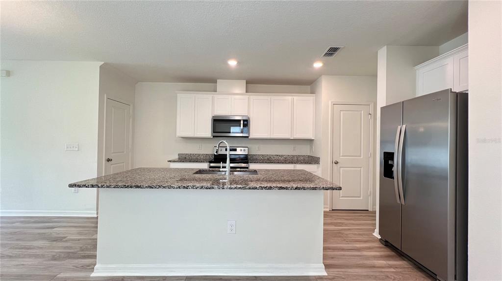 A kitchen features white cabinets, granite countertops, a center island, and stainless steel appliances — 1340 MIRABELLA CIRCLE, DAVENPORT, FL