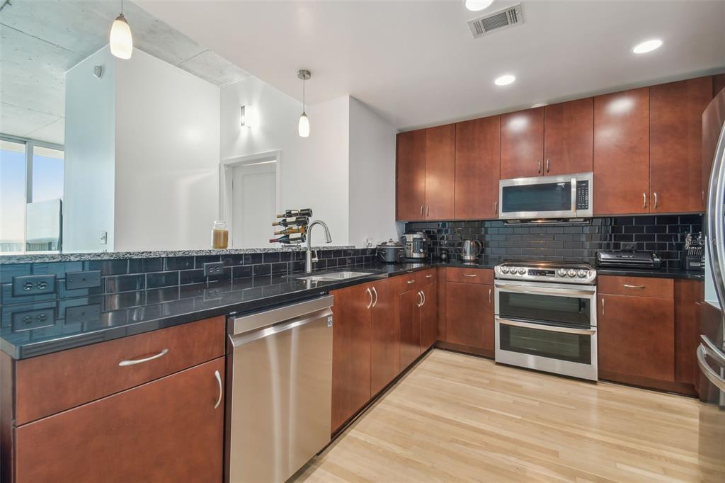 A kitchen features wood cabinets, black countertops, a black subway tile backsplash, and stainless appliances — 777 N ASHLEY DRIVE UNIT 3009, TAMPA, FL