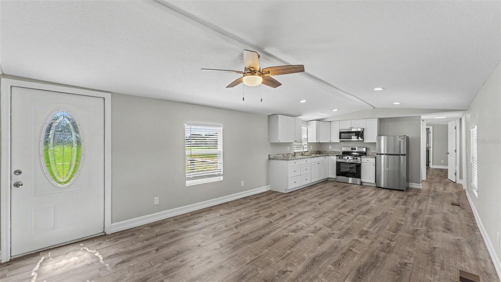 An open-concept kitchen and living area features light gray walls, wood-look flooring, and white cabinetry — 21 RIDGE ROAD, FROSTPROOF, FL