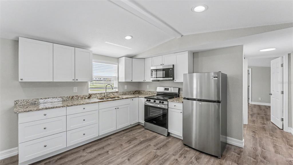A kitchen features white cabinets, granite countertops, stainless steel appliances, and wood-look flooring — 21 RIDGE ROAD, FROSTPROOF, FL
