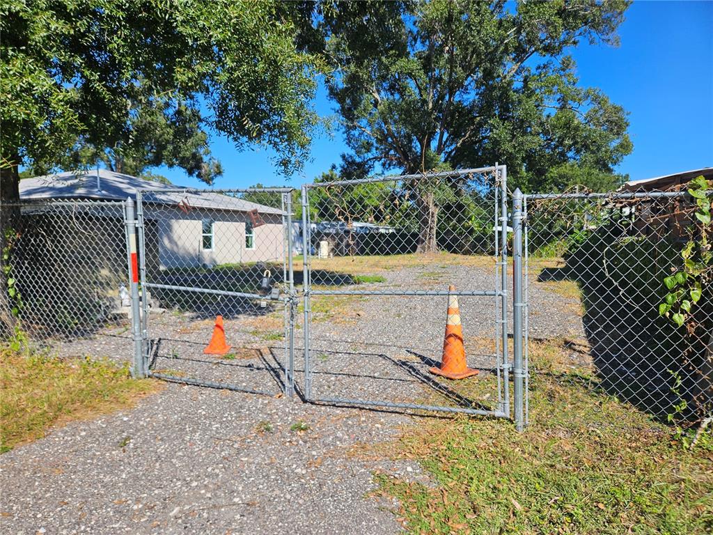 A gravel driveway leads to a chain-link fence with two orange traffic cones — 12321 CAMBRIDGE AVENUE, TAMPA, FL