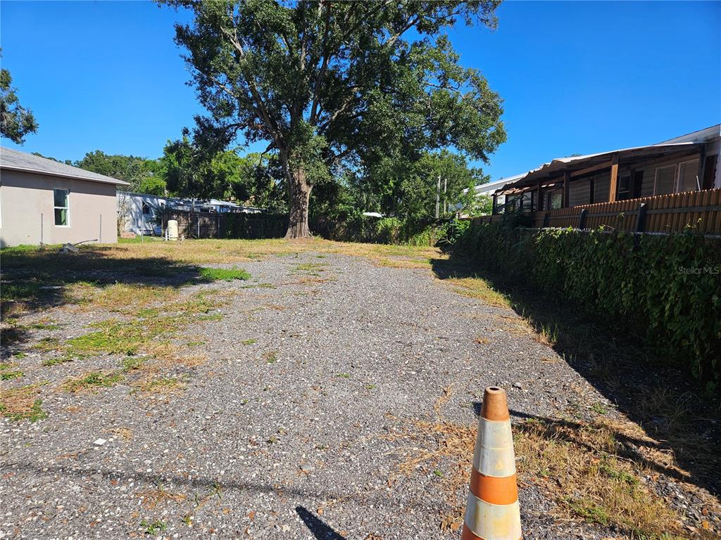 A gravel lot features a large tree in the background with buildings on both sides — 12321 CAMBRIDGE AVENUE, TAMPA, FL