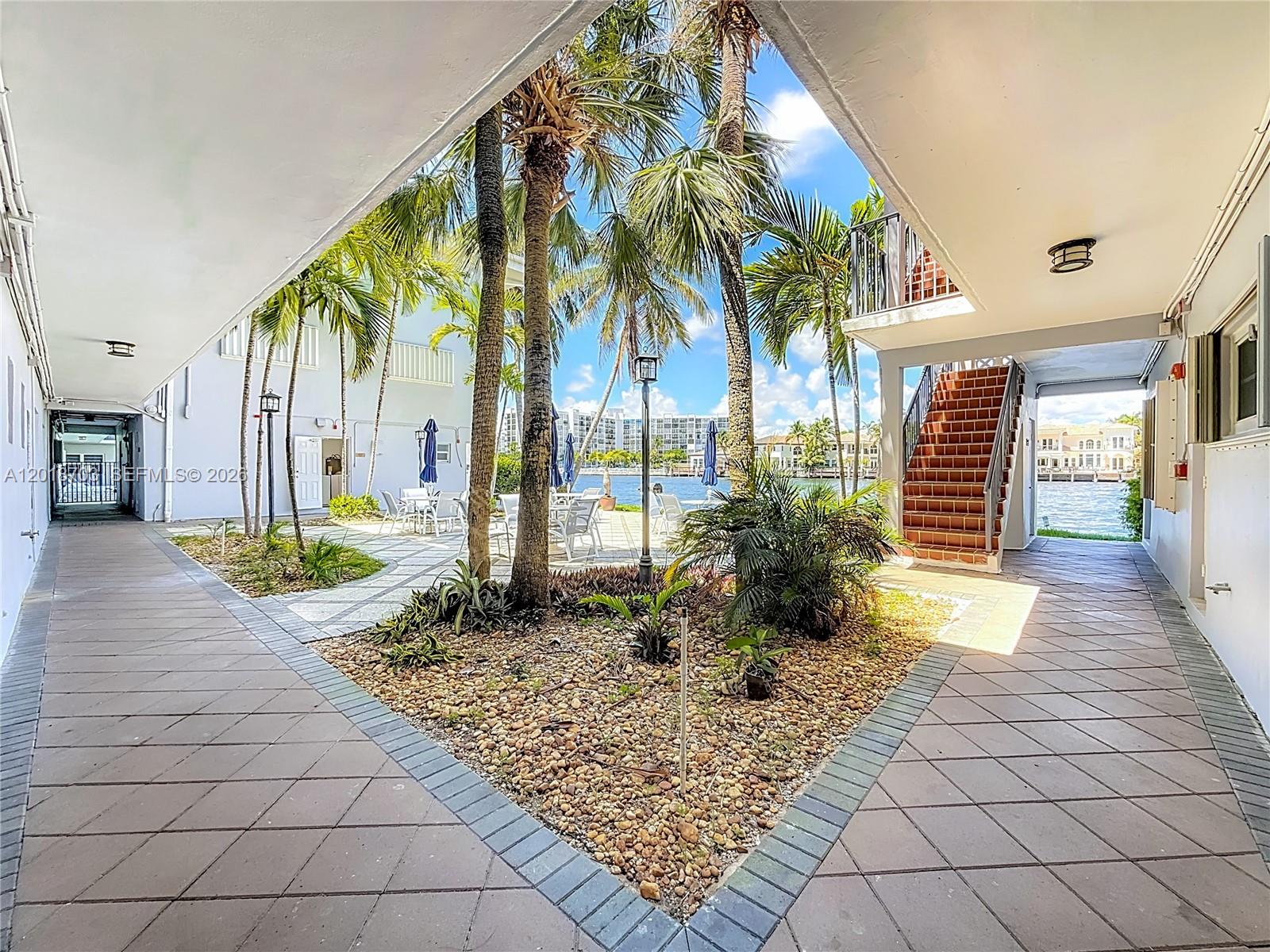 A paved courtyard with palm trees and a staircase leads to a waterfront view — 2600 S Ocean Dr # S102, Hollywood FL 33019, HOLLYWOOD, FL