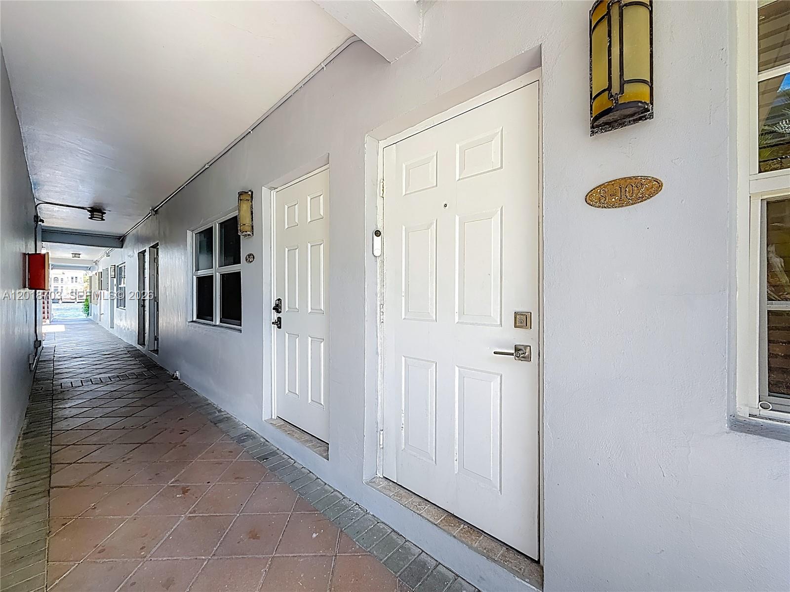 An outdoor walkway features white doors, tiled flooring, and wall-mounted light fixtures — 2600 S Ocean Dr # S102, Hollywood FL 33019, HOLLYWOOD, FL