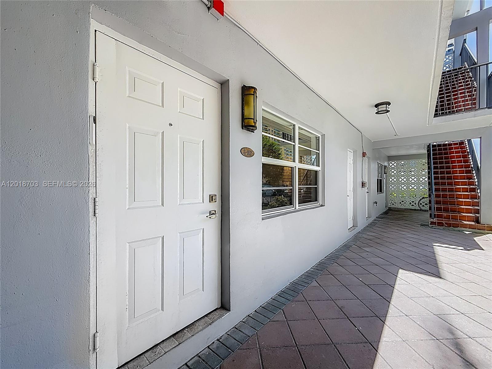 A white door with a window and a light fixture sits along an outdoor walkway — 2600 S Ocean Dr # S102, Hollywood FL 33019, HOLLYWOOD, FL