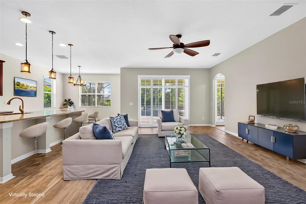 A living room and kitchen area with light wood floors, a sofa, and a television — 3938 90TH AVENUE E, PARRISH, FL