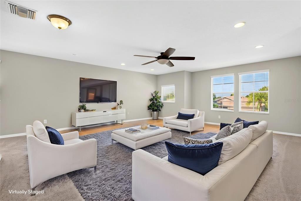 A virtually staged living room features a large gray rug, white furniture, and a television — 3938 90TH AVENUE E, PARRISH, FL