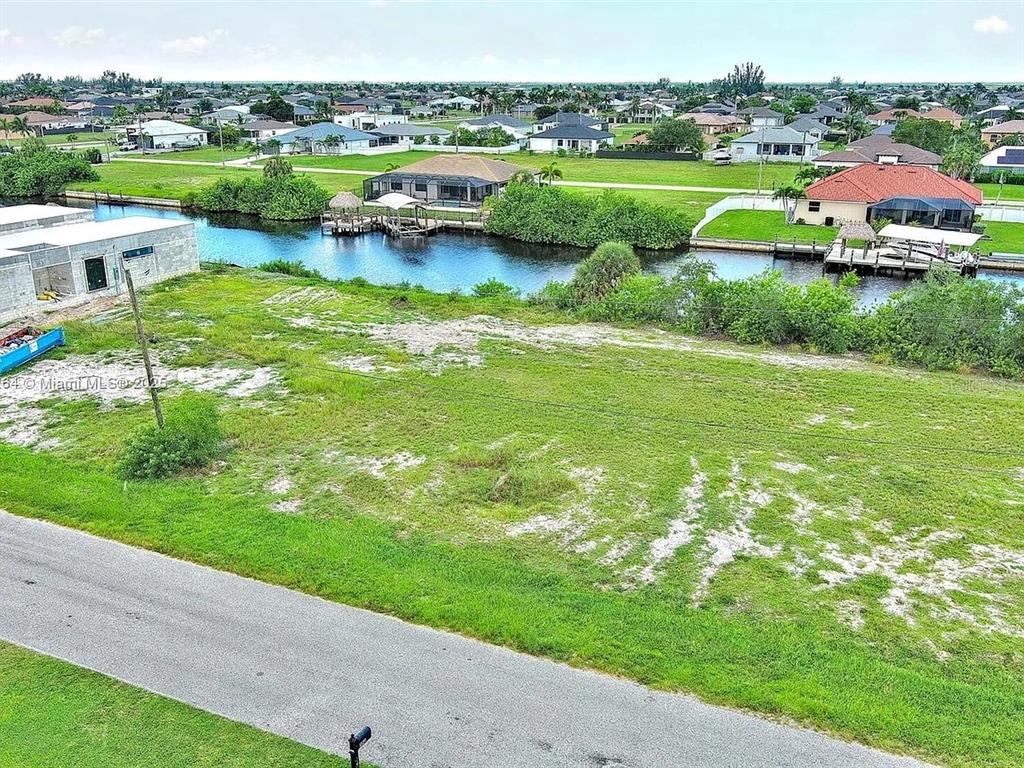 An aerial view shows a vacant grassy lot bordering a canal with nearby residential homes — 1228 NW 34TH AVENUE, CAPE CORAL, FL