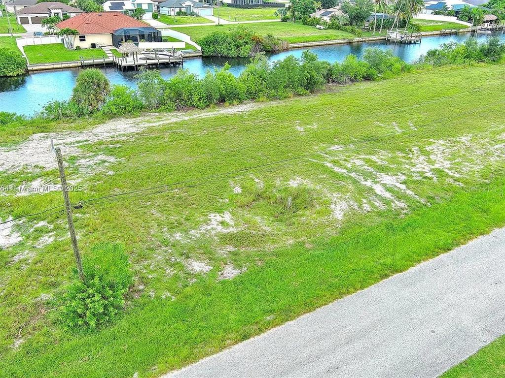 An aerial view shows a vacant grassy lot adjacent to a canal and residential homes — 1228 NW 34TH AVENUE, CAPE CORAL, FL