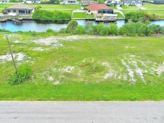 An elevated view shows a vacant grassy lot bordering a canal with nearby residential homes — 1228 NW 34TH AVENUE, CAPE CORAL, FL