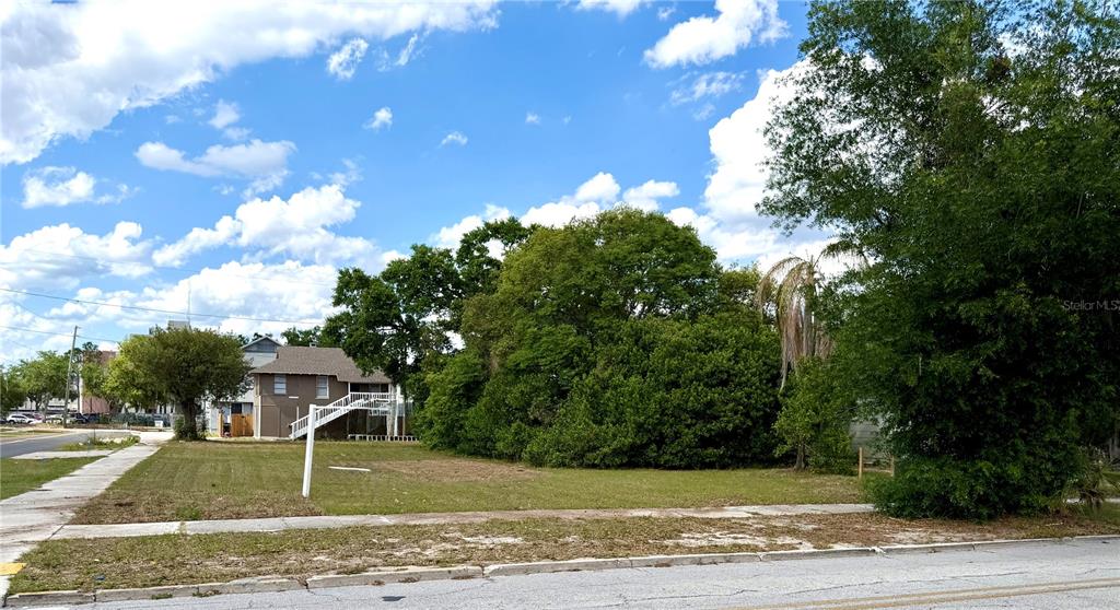 A vacant grassy lot sits next to a two-story house with an exterior staircase — 203 AVENUE C NE, WINTER HAVEN, FL