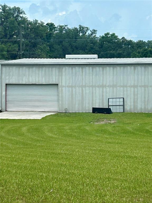 A metal storage building features a roll-up garage door and a window leaning against the wall — 19808 N US HIGHWAY 441, HIGH SPRINGS, FL