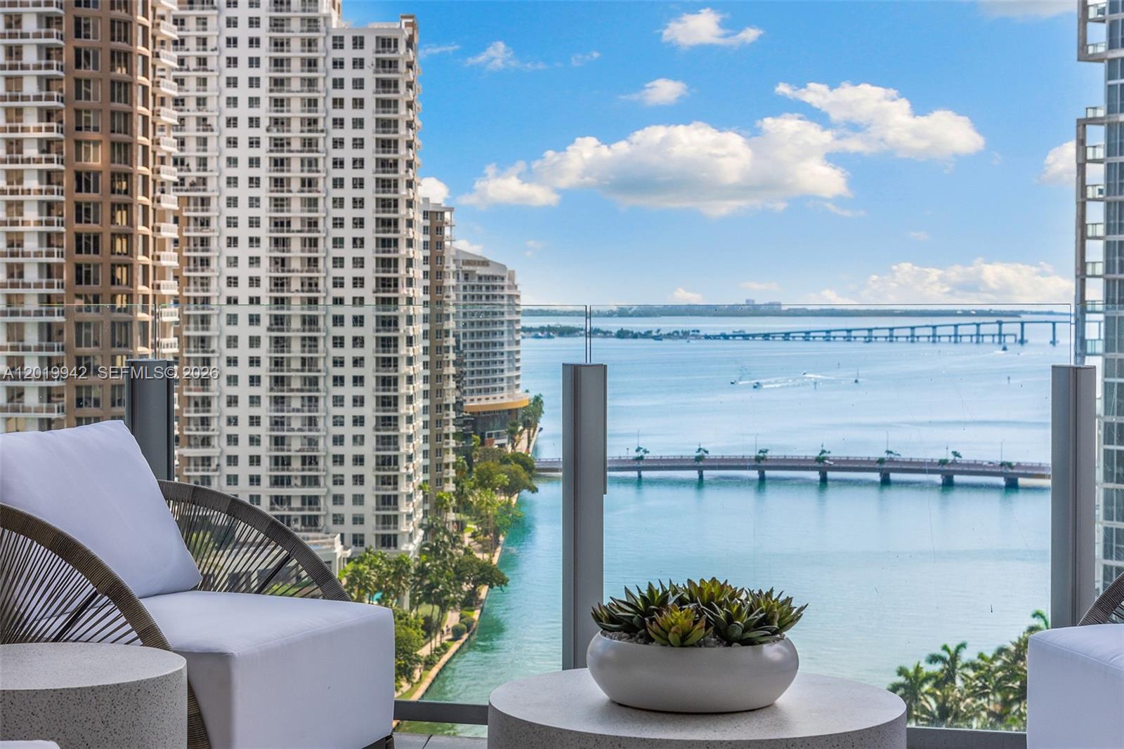 A balcony with outdoor seating overlooks a bay, a bridge, and high-rise apartment buildings — 300 Biscayne Blvd Way # 1605, Miami FL 33131, MIAMI, FL