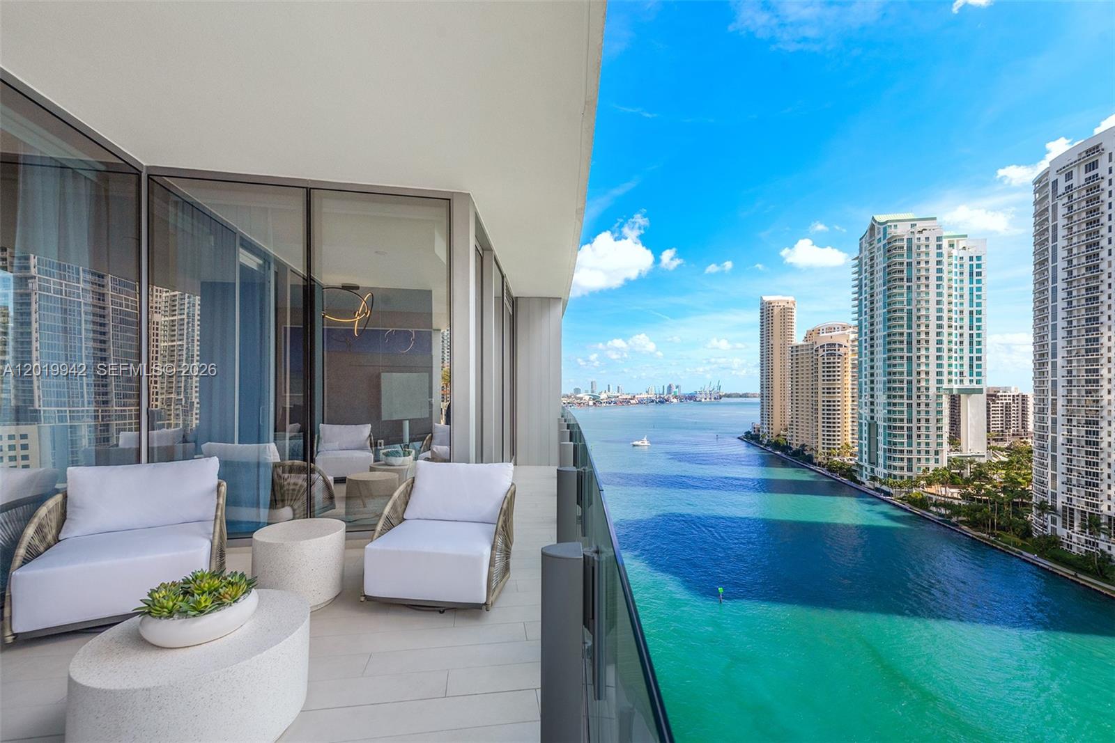 A high-rise balcony features white lounge chairs and tables overlooking a bay and city skyline — 300 Biscayne Blvd Way # 1605, Miami FL 33131, MIAMI, FL