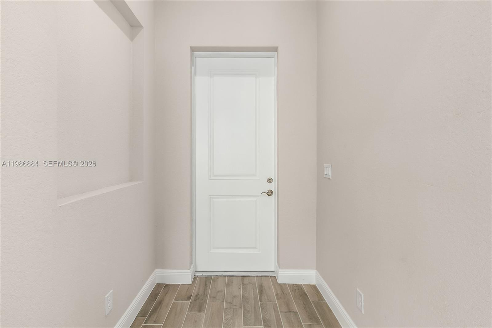 A white door is centered in a hallway with light walls and wood-look tile flooring — 206 Jubilee Terr, La Belle FL 33935, LA BELLE, FL