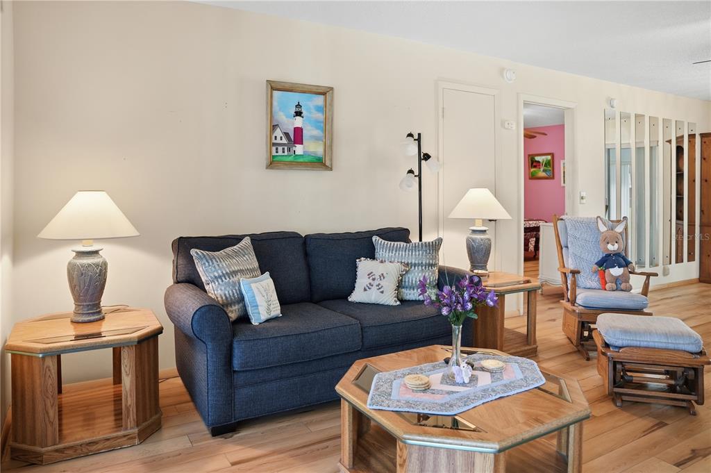 A living room features a blue sofa, wooden tables, a lighthouse painting, and hardwood floors — 103 LUCA LANE, KISSIMMEE, FL