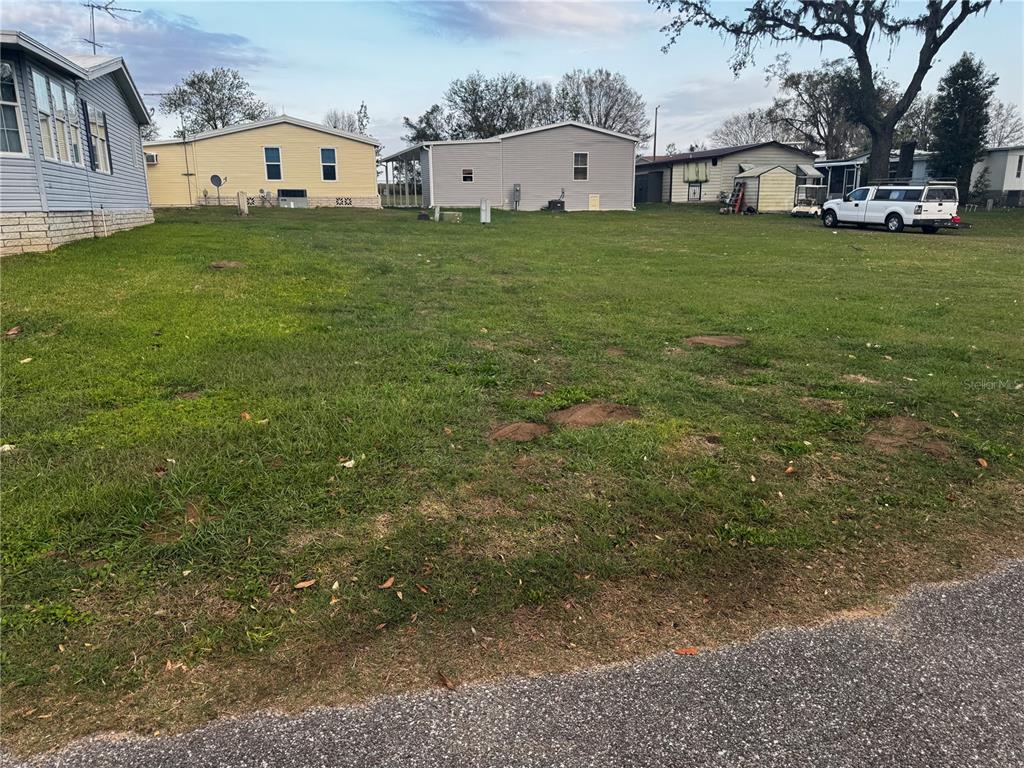 A vacant grassy lot sits between several manufactured homes under a clear sky — 10024 WELLINGTON AVENUE, DADE CITY, FL