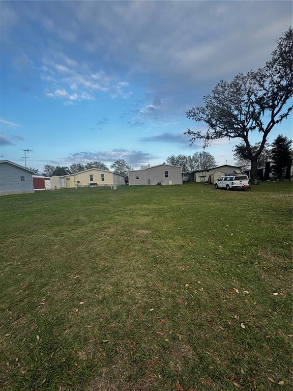 A large, grassy vacant lot is surrounded by several single-story residential buildings and a parked truck — 10024 WELLINGTON AVENUE, DADE CITY, FL