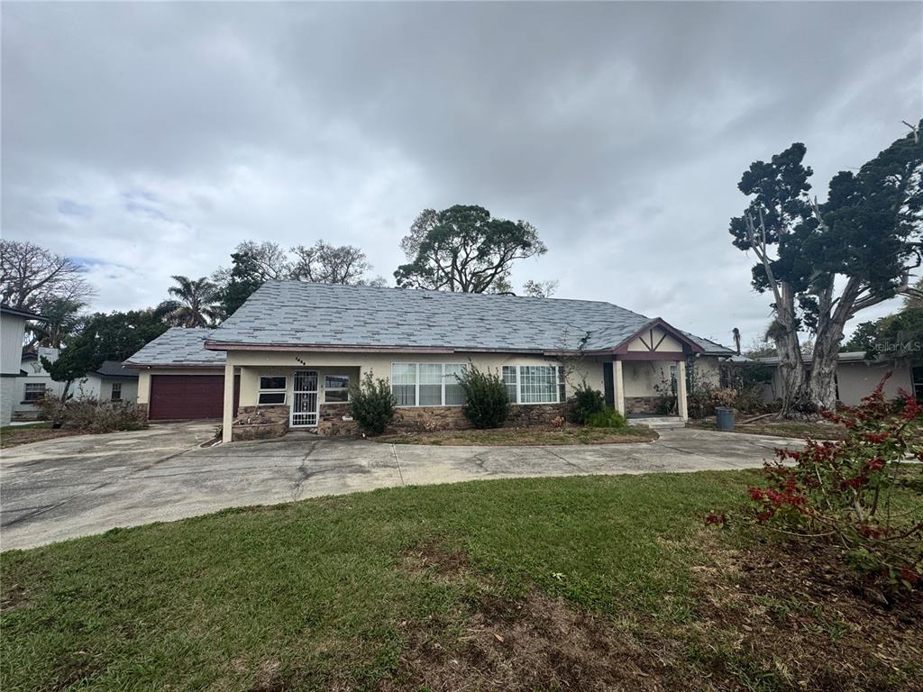 A single-story house with a gray shingled roof, stone accents, and a large concrete driveway — 1450 W LAKE CANNON DRIVE NW, WINTER HAVEN, FL