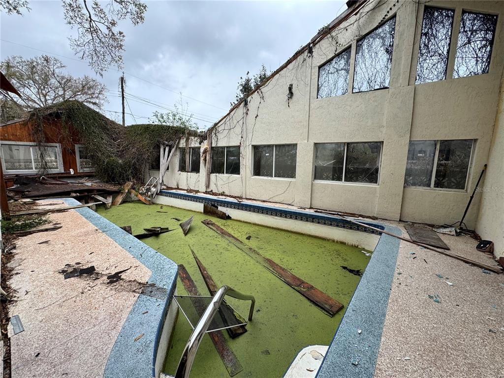 A neglected swimming pool filled with green water sits beside a weathered, multi-story stucco house — 1450 W LAKE CANNON DRIVE NW, WINTER HAVEN, FL