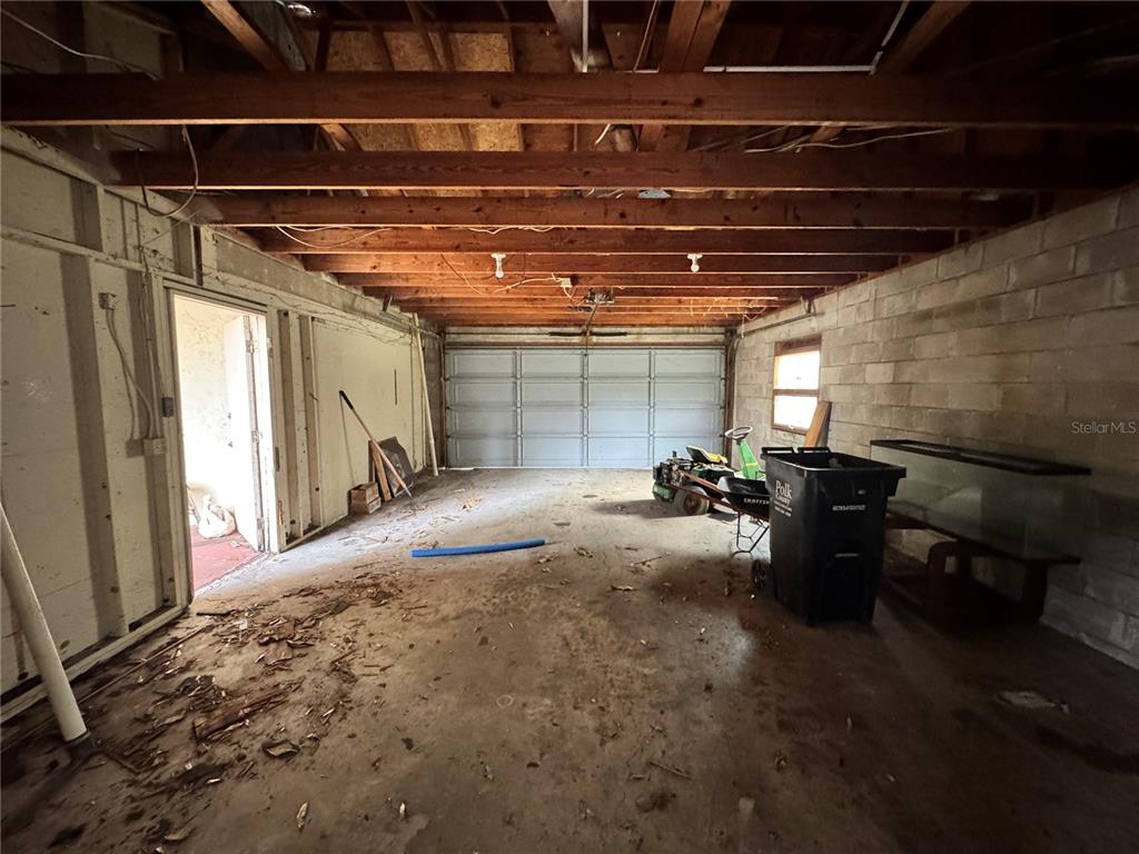 An unfinished garage features exposed wooden ceiling beams, concrete block walls, and a concrete floor — 1450 W LAKE CANNON DRIVE NW, WINTER HAVEN, FL