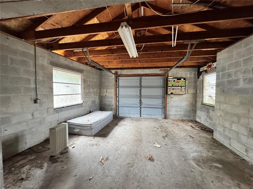 An unfinished garage with concrete block walls, a concrete floor, and an exposed wood ceiling — 1450 W LAKE CANNON DRIVE NW, WINTER HAVEN, FL