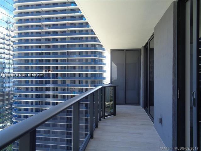 A balcony with a metal railing overlooks a tall, modern glass skyscraper — 45 SW 9th St # 2709, Miami FL 33130, MIAMI, FL
