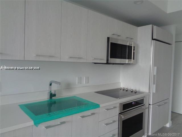 A modern kitchen features light wood cabinets, stainless steel appliances, and a sink with protective film — 45 SW 9th St # 2709, Miami FL 33130, MIAMI, FL
